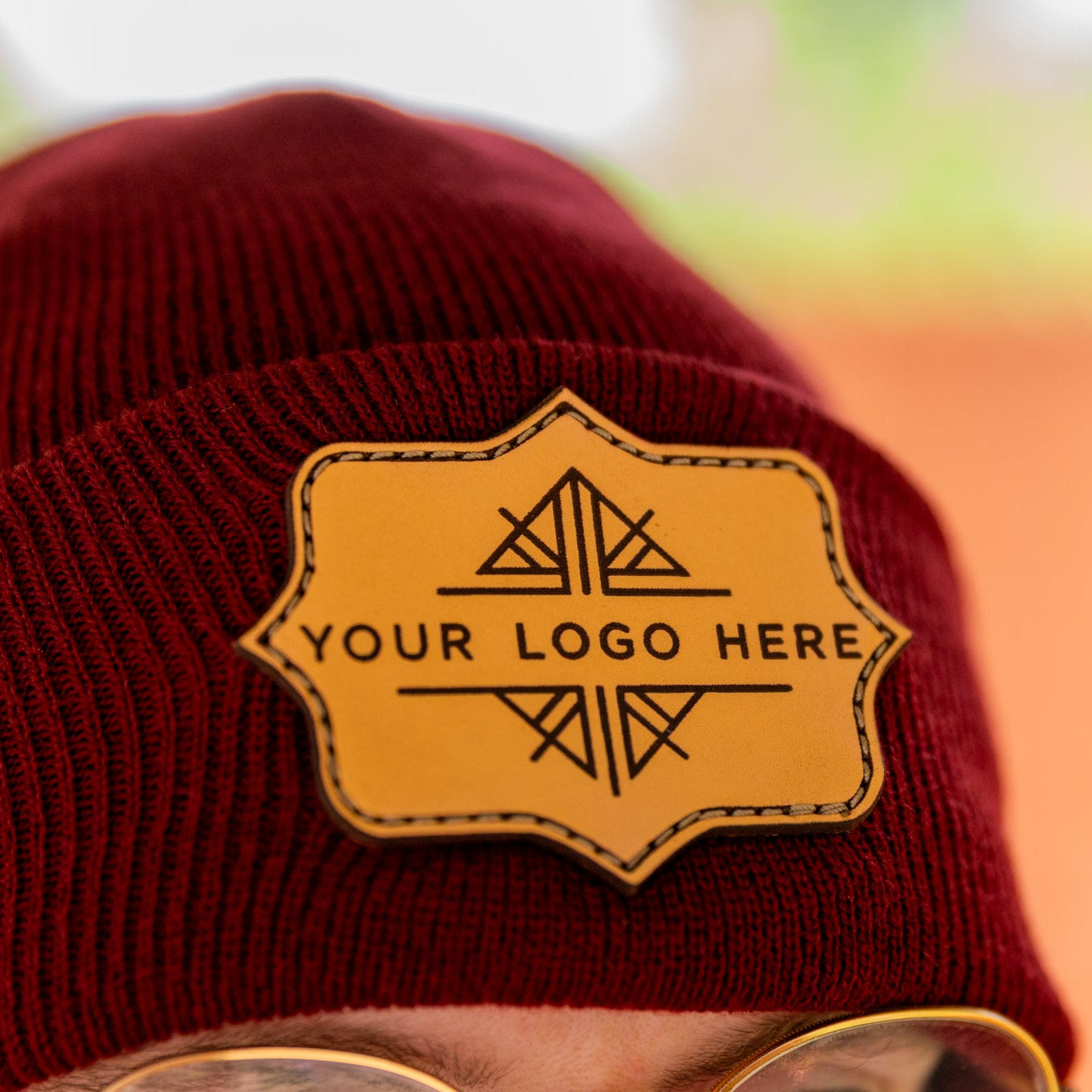 Red beanie with a yellow patch labeled 'Your Logo Here' against a blurred background