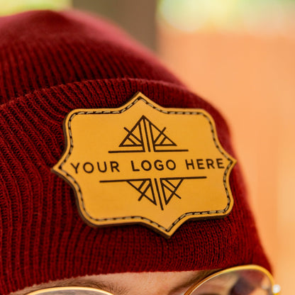 Red beanie with a customizable logo patch worn by a person, with a blurred background.